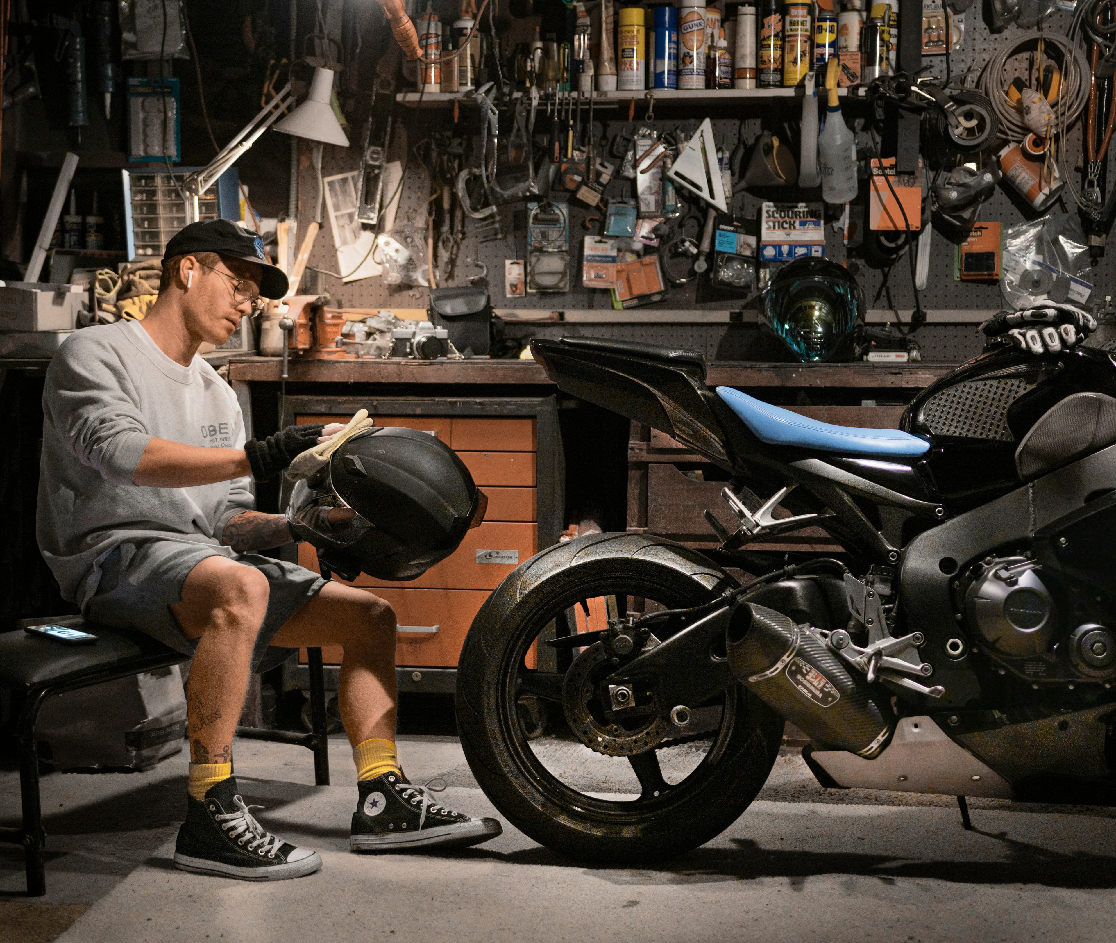 Rider cleaning a helmet next to a motorcycle in a garage