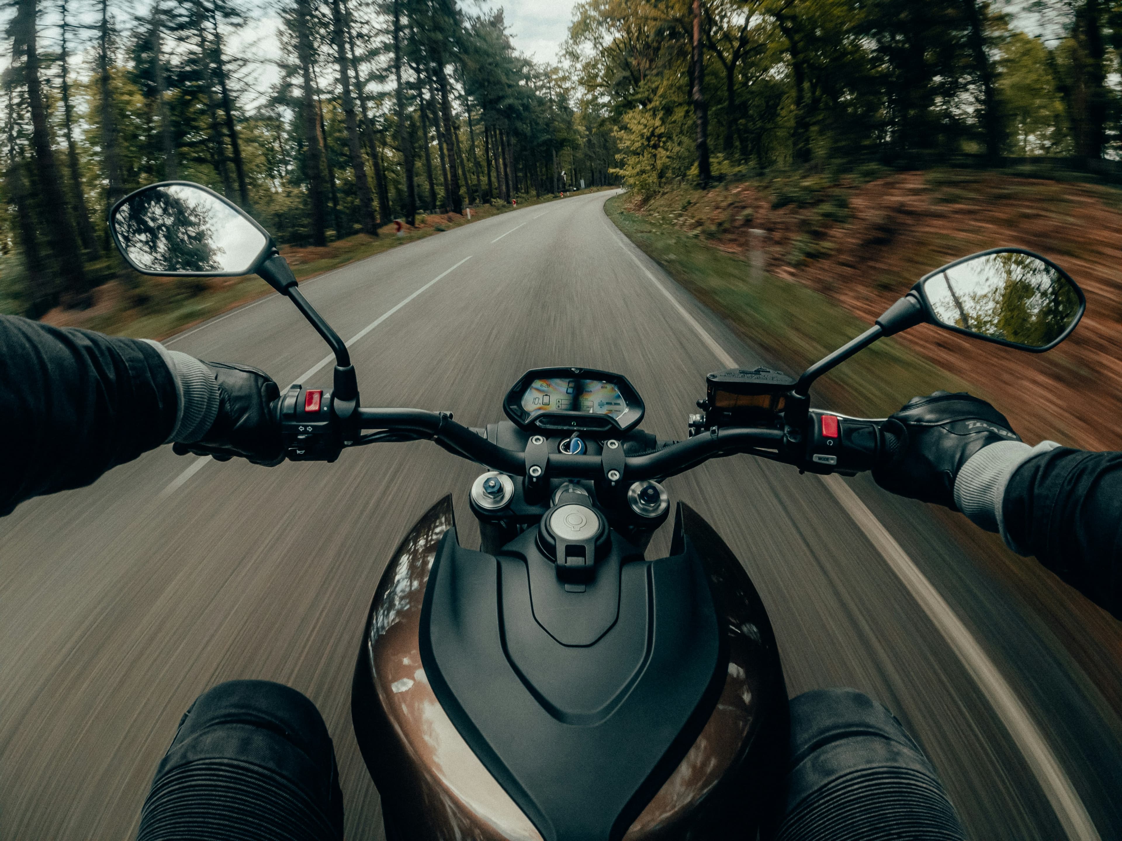 Gloved hands on motorcycle handlebars on a forest road
